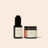 A skincare set from Faithful Skin Shop featuring an ozonated facial serum in a dark amber bottle with a black dropper cap, and an ozonated facial balm in a dark amber jar with a black lid, both with cream labels on a light beige background.